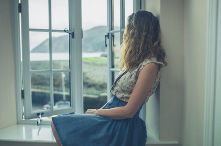 A young woman is sitting by the window of a rural home