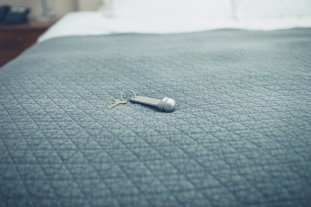 A hotel room key on a freshly made bedの写真素材