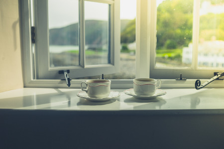 Two cups of tea or coffee by the window on a sunny day in a rural homeの写真素材