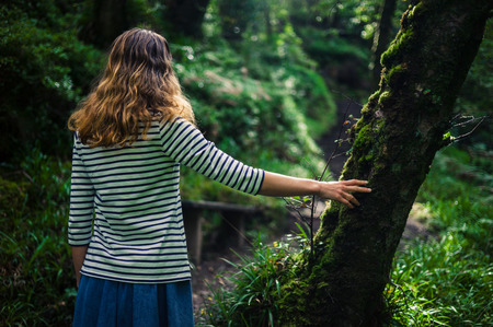 A young woman is resting her hand on a tree in  the forestの写真素材