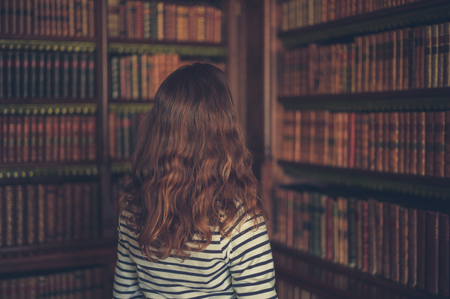 A young woman is looking at the books on the shelves in an old libraryの写真素材