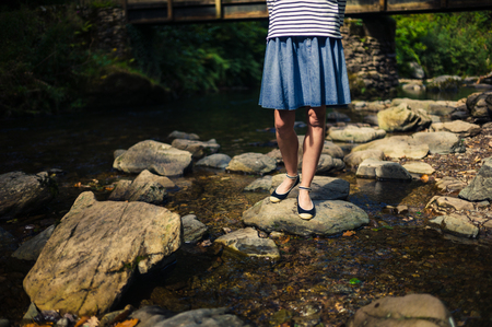 A young woman wearing a skirt is standing on some rocks in the river on a summer dayの写真素材