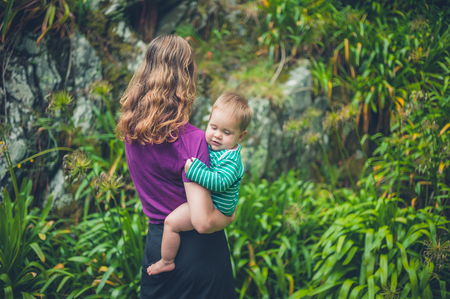 A young mother is standing outside holding her baby in natureの写真素材