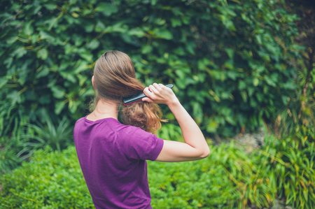 A young woman is brushing her hair outside in natureの写真素材