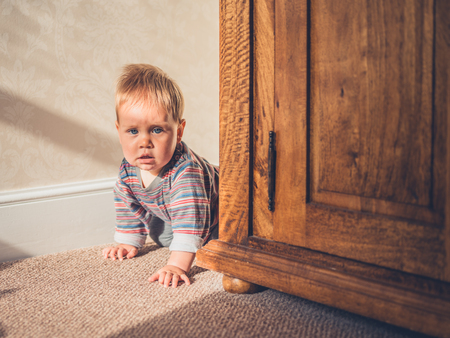 A cute little baby is crawling on the floor behind a wardrobeの写真素材