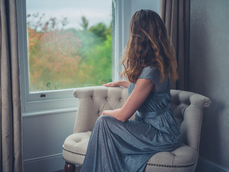 A young woman wearing an elegant dress is daydreaming by the windowの写真素材