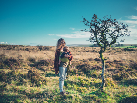 A young mother is standing by a tree in the wilderness with her baby in a slingの写真素材