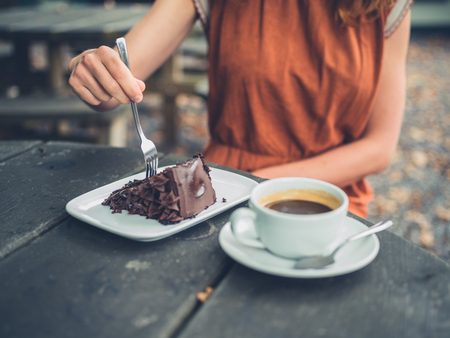 A young woman is sitting outside drinking coffee and eating cakeの写真素材