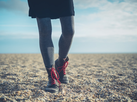 The legs of a young woman wearing boots walking on the beach in the autumnの写真素材