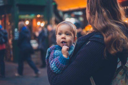 A young mother is standing in the street with her baby in a sling