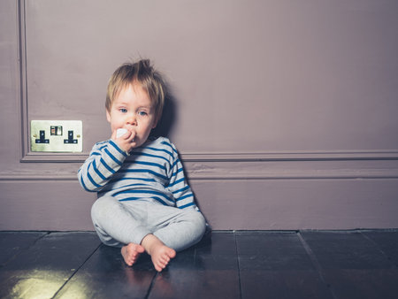 A cute little boy is sitting on the floor chewing on an electric adapter