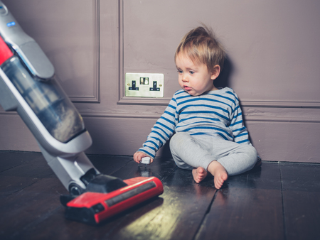 A cute little boy is sitting on the floor and is surprised by the vacuum cleanerの写真素材