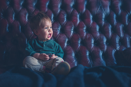 A cute little boy is sitting on a leather sofa with a toy car in his handの写真素材