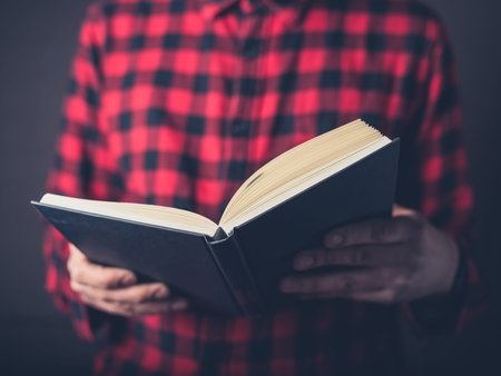 A young man wearing a flannel shirt is reading a book