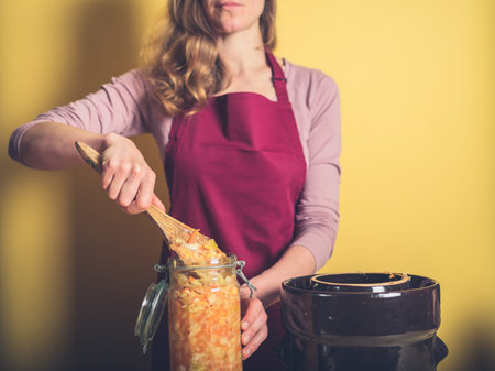 A young woman is removing her delicious and nutritious homemade kimchi from a fermentation pot