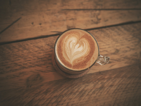 Cup of coffee with heart shaped froth on wooden tableの写真素材