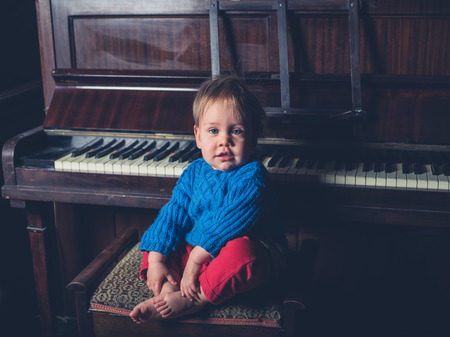 A cute little baby boy is sitting by a pianoの写真素材