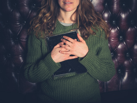 A happy young woman sitting on a sofa is clutching a picture frameの写真素材
