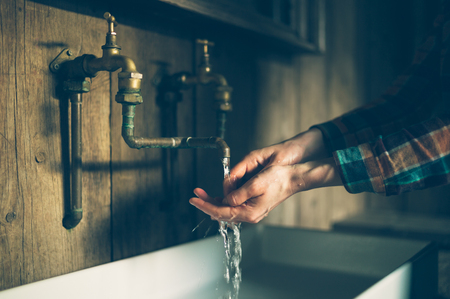 A young woman is washing her hands in a sink with brass faucetsの写真素材
