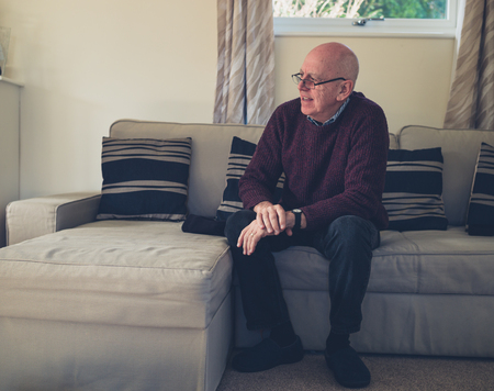A senior man is sitting on a sofa indoorsの写真素材
