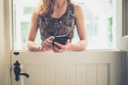 A young woman is standing by a stable door and is using her smart phoneの写真素材