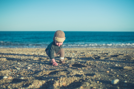 A cute little toddler is playing on the beach in winterの写真素材