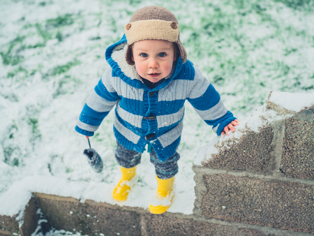 A scute little boy is standing in the snowの写真素材