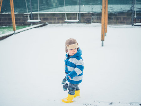 A little toddler is exploring a playground in the snowの写真素材