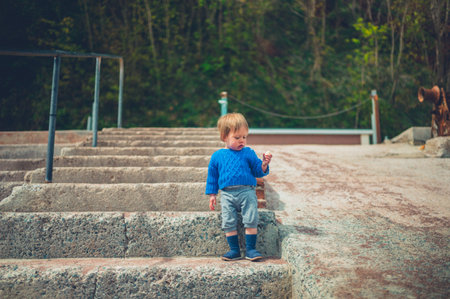 A little boy is eating banana on concrete steps outdoorsの写真素材