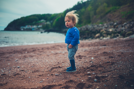 A cute little toddler boy is on the beach on a cold dayの写真素材