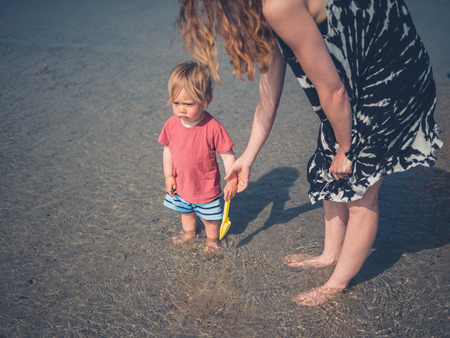 A young mother is walking on the beach with her little toddlerの写真素材