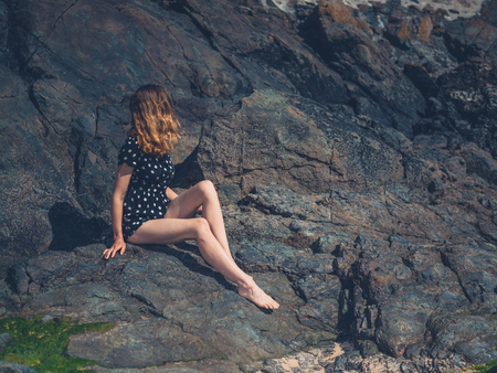 A young woman is sitting on some rocks in the summerの写真素材