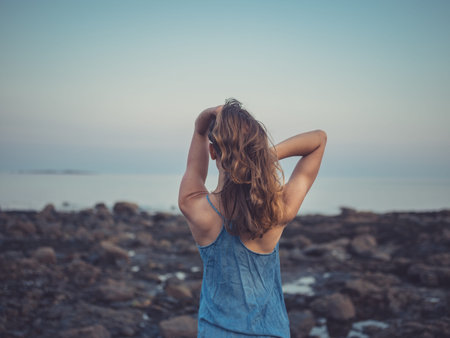 A young woman is standing on the coast at sunset