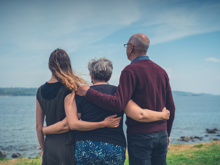 A senior couple with their adult daughter are standing by the seaの写真素材