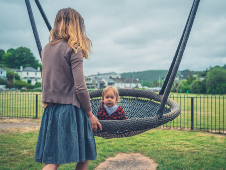 A young mother is pushing her toddler on a swing at the playground