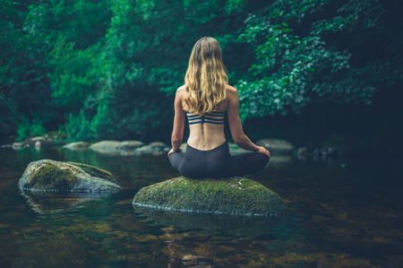A young woman is meditating on a rock in the riverの写真素材