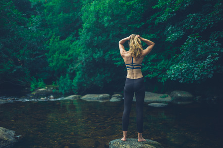 A young fitness woman is standing on a rock in the riverの写真素材