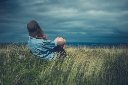 A young woman is sitting in a field on a windy dayの写真素材