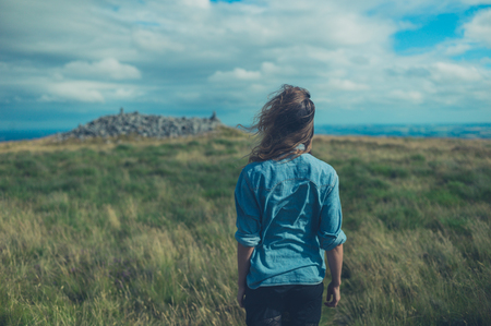 A young woman is standing in a field on a windy dayの写真素材