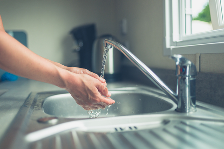 A young woman is washing her hands in the kitchen sinkの写真素材