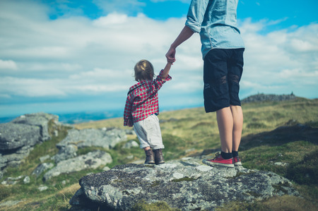 A young mother and her little toddler are admiring the view from the top of a rock on a hill in the moorの写真素材