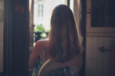A young woman is sitting in a kitchen by the balconyの写真素材
