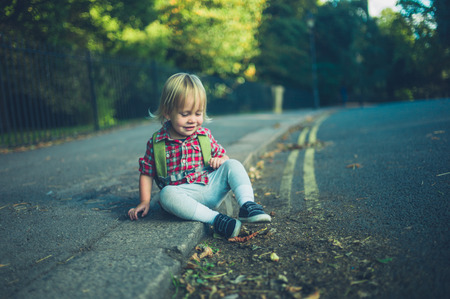 A little toddler is sitting on the sidewalk in a park on an autumn dayの写真素材