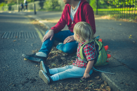 A little toddler and his father are relaxing on the sidewalk in a park in autumnの写真素材
