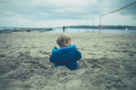 A little toddler is dressed up warm for a day on the beach in autumnの写真素材
