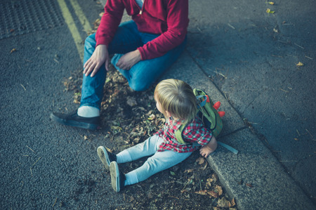 A little toddler and his father are relaxing on the sidewalk in a park in autumnの写真素材