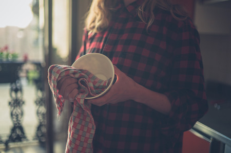 A young woman is drying the dishes in her kitchenの写真素材