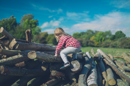A little toddler is climbing on some logs in the forestの写真素材