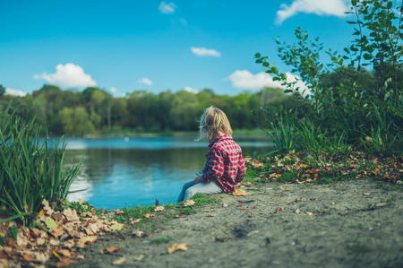 A little toddler is sitting by the pond in a forestの写真素材