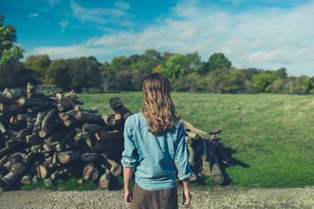 A young woman is standing by a pile of logs in the forest in the autumnの写真素材